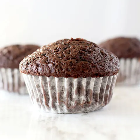 three chocolate muffins on a white counter