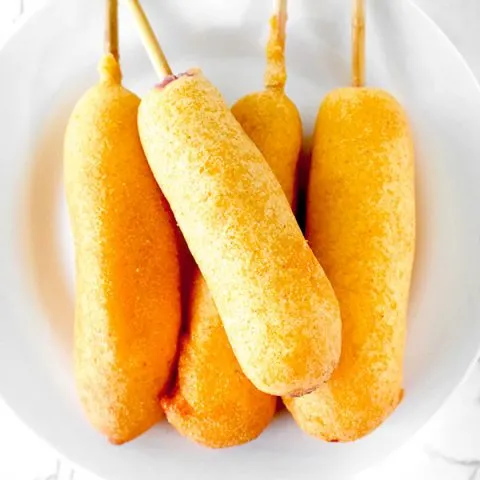 four corn dogs on a white plate