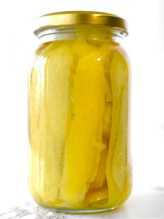 Lemon peals in a jar with vadka on a white marble counter