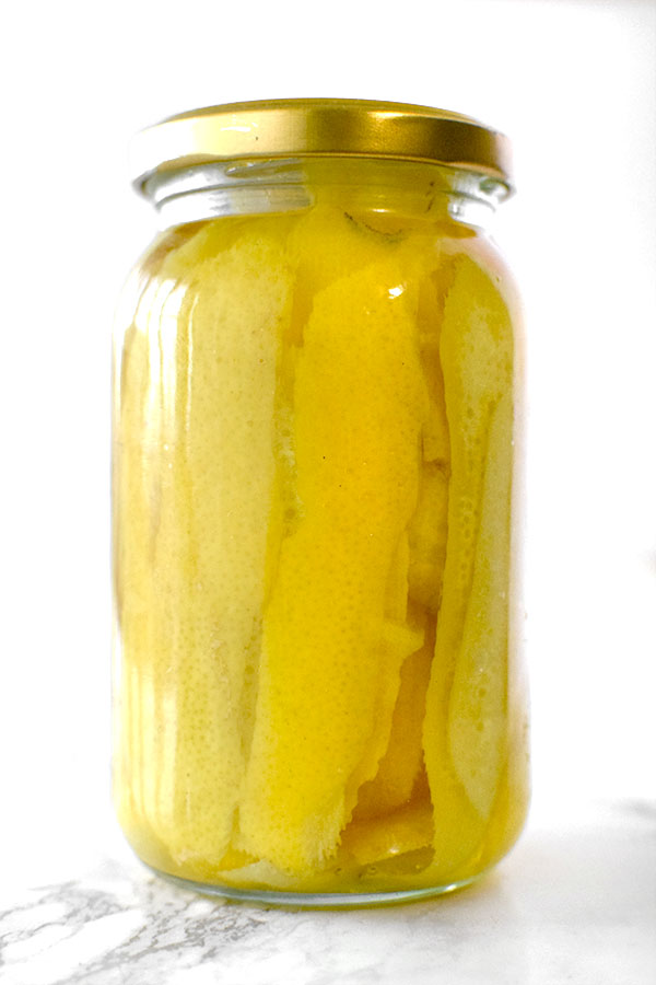 Lemon peals in a jar with vadka on a white marble counter