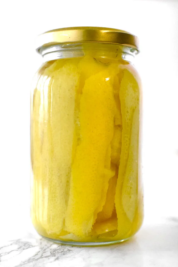 Lemon peals in a jar with vadka on a white marble counter