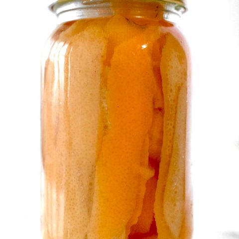 Orange peals in a jar with vadka on a white marble counter