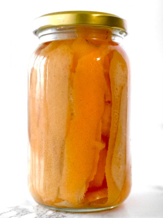 Orange peals in a jar with vadka on a white marble counter