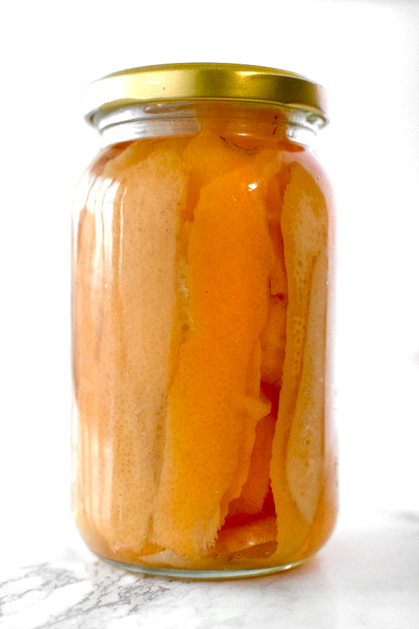 Orange peals in a jar with vadka on a white marble counter