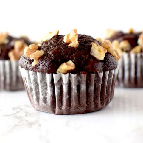 three chocolate walnut muffins on a white marble counter