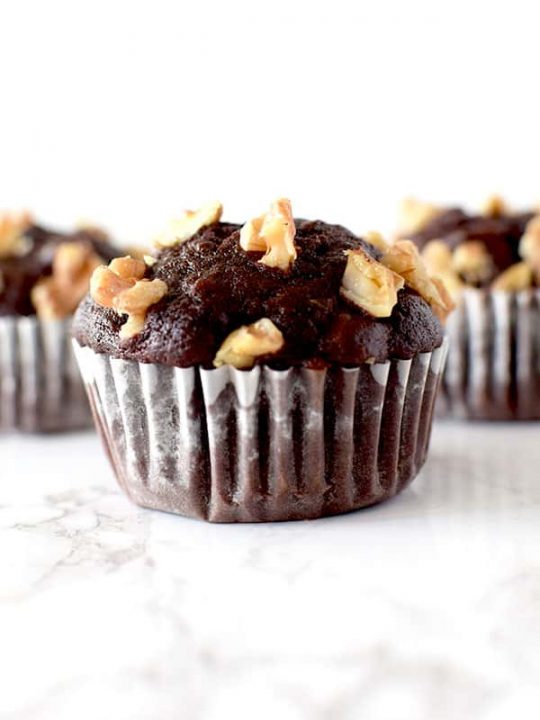 three chocolate walnut muffins on a white marble counter