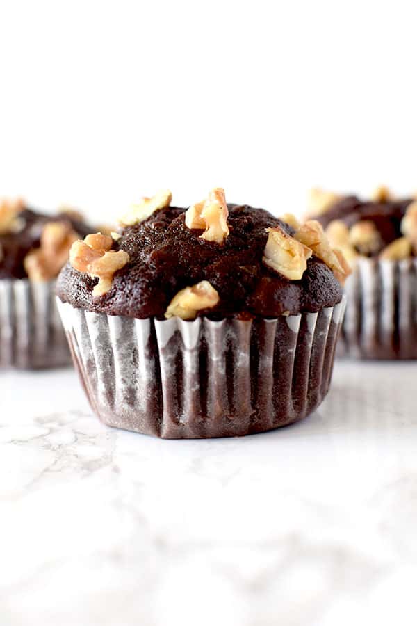 three chocolate walnut muffins on a white marble counter