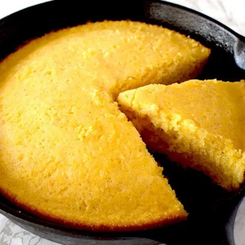 Cornbread in a cast iron skillet with a piece missing