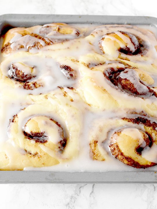 Six glazed no knead cinnamon rolls in a baking pan