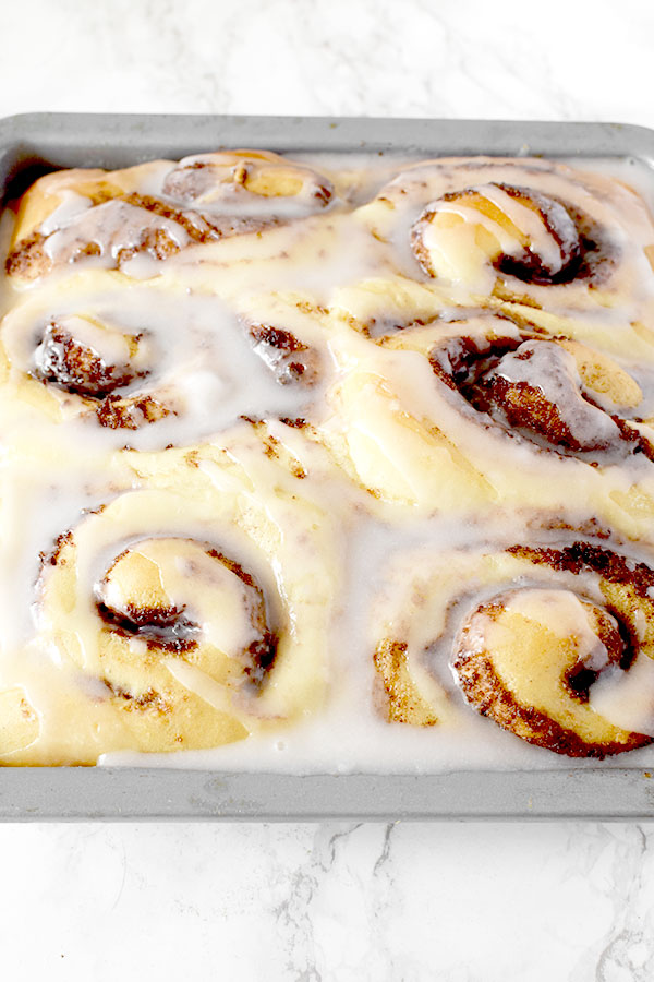 Six glazed no knead cinnamon rolls in a baking pan