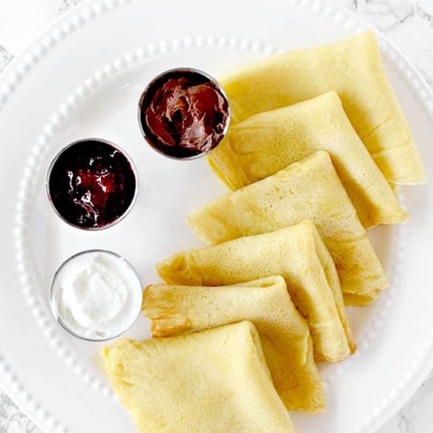 Dairy free crepes on a plate with jam, Nutella, and cream