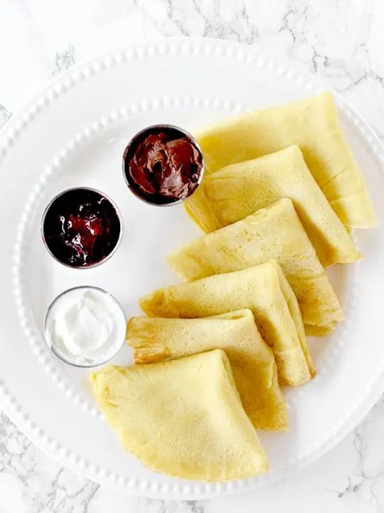 Dairy free crepes on a plate with jam, Nutella, and cream