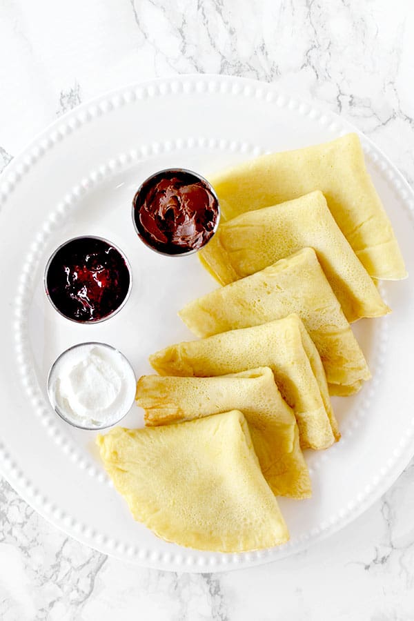 Dairy free crepes with almond milk on a plate with jam, Nutella, and cream