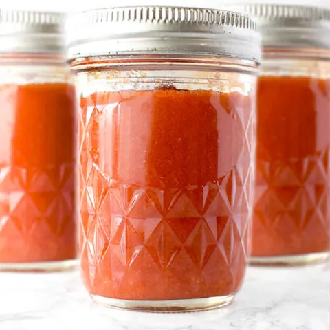 three mason jars of salsa roja on a white marble counter