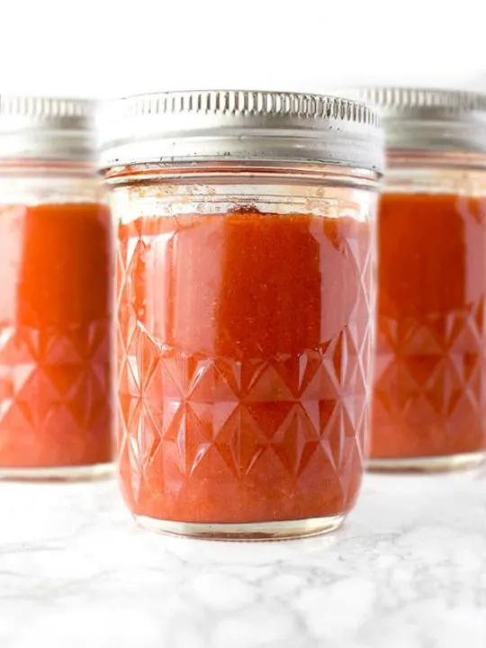 three mason jars of salsa roja on a white marble counter