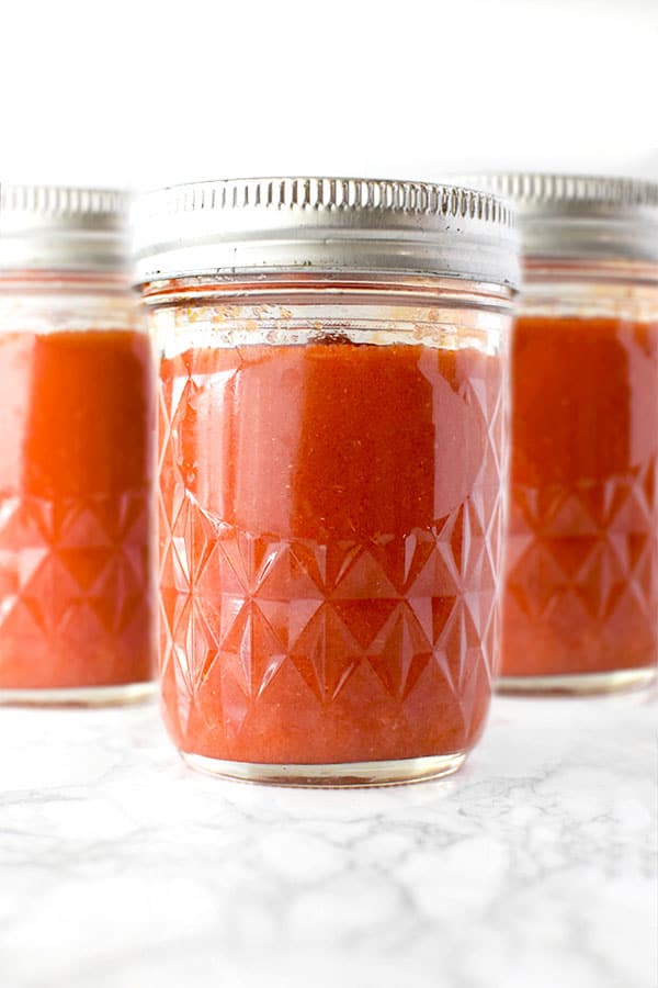 three mason jars of salsa roja on a white marble counter