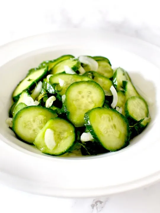 cucumber salad in a white bowl on a white marble counter