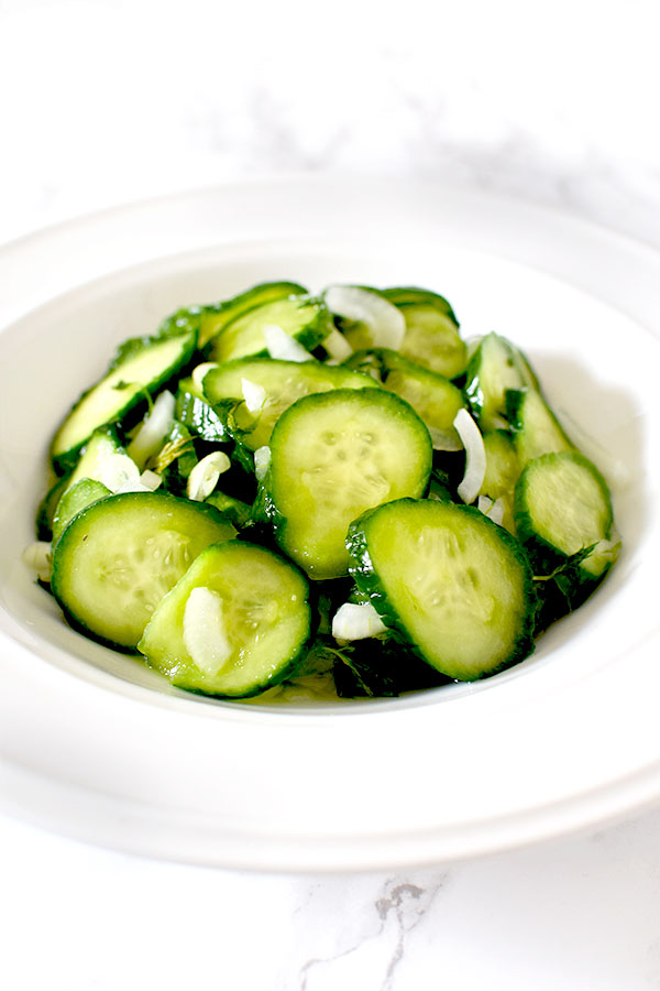 cucumber salad in a white bowl on a white marble counter