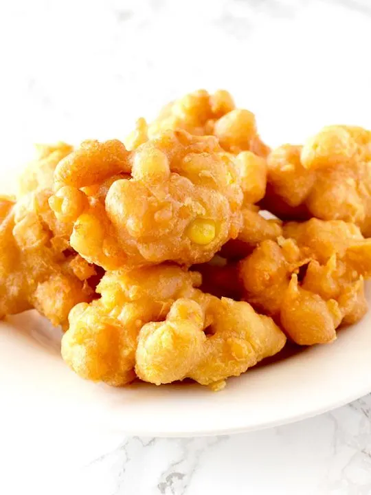 Corn fritters on a white plate on a white marble counter