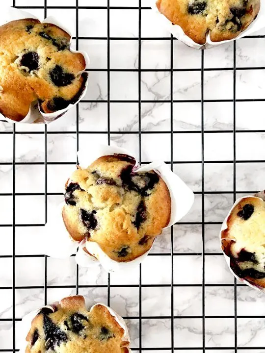 blueberry muffins on a black cooling rack on a white marble counter