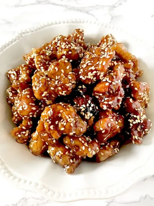 Chinese sesame chicken in a white bowl on a white marble counter