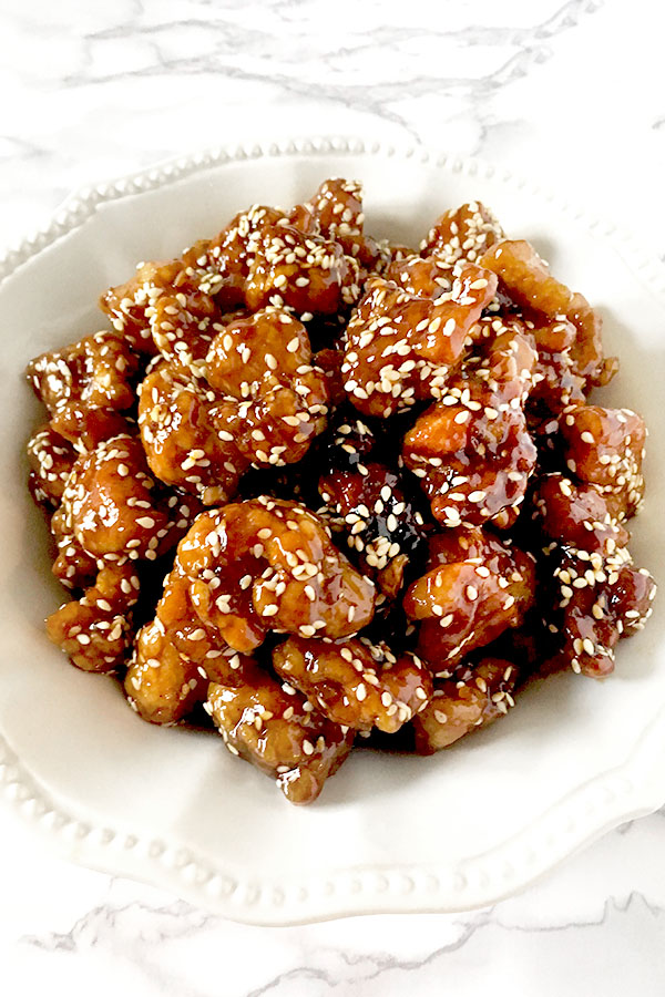 Chinese sesame chicken in a white bowl on a white marble counter