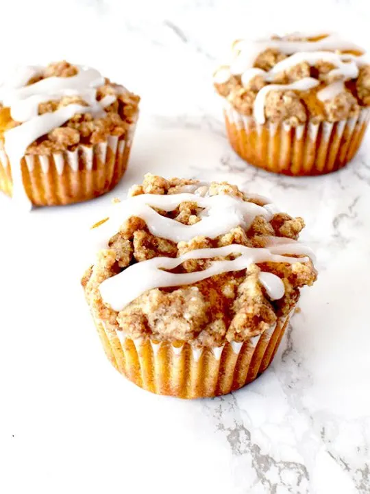 pumpkin muffins with streusel and icing on a white marble counter