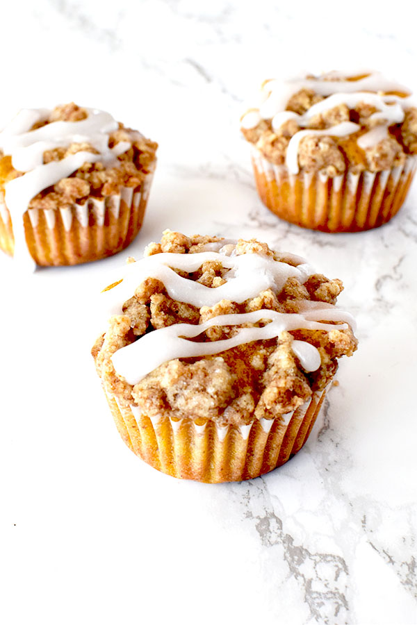 pumpkin muffins with streusel and icing on a white marble counter