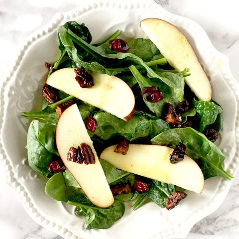 Apple cranberry salad featuring sliced apples on a bed of baby spinach topped with cranberries and nuts