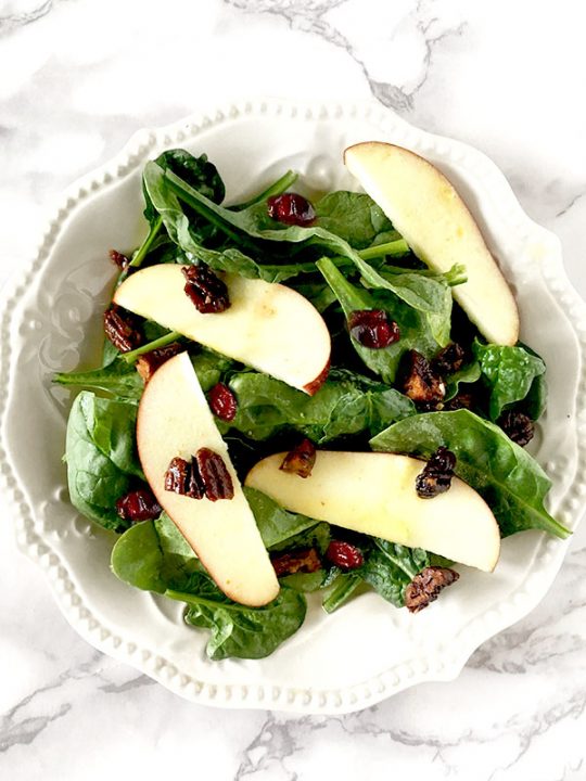 Apple cranberry salad featuring sliced apples on a bed of baby spinach topped with cranberries and nuts