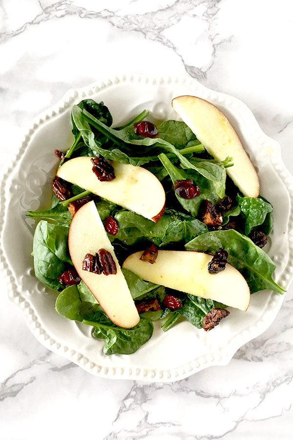 Apple cranberry salad featuring sliced apples on a bed of baby spinach topped with cranberries and nuts