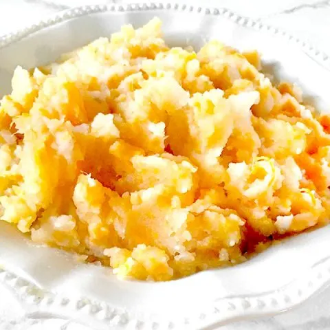 Mixed mashed potatoes in a white bowl on a white marble counter