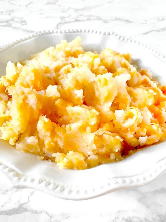 Mixed mashed potatoes in a white bowl on a white marble counter