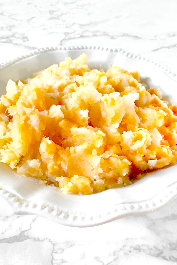 Mixed mashed potatoes in a white bowl on a white marble counter