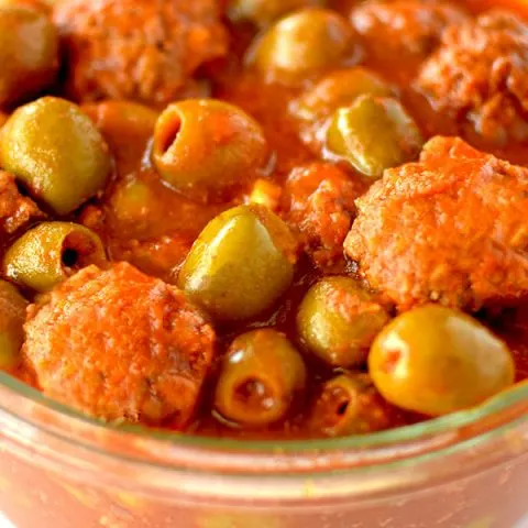 Glass bowl filled with meatballs and olives in tomato sauce