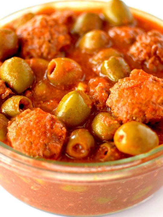 Glass bowl filled with meatballs and olives in tomato sauce