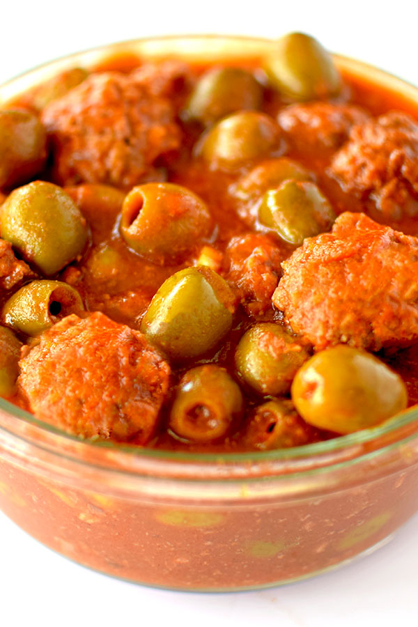 Glass bowl filled with meatballs and olives in tomato sauce