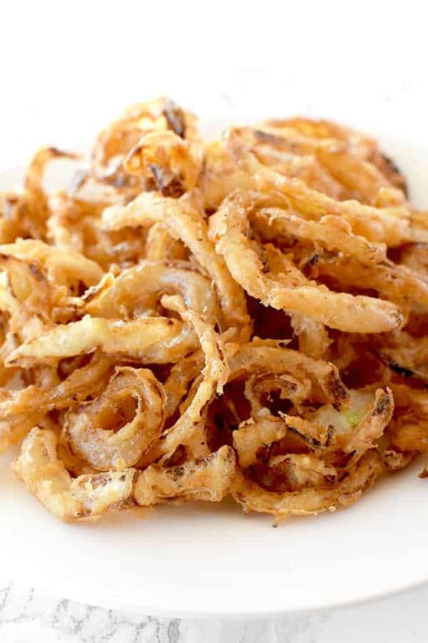 Homemade fried onions on a white plate on a white marble counter