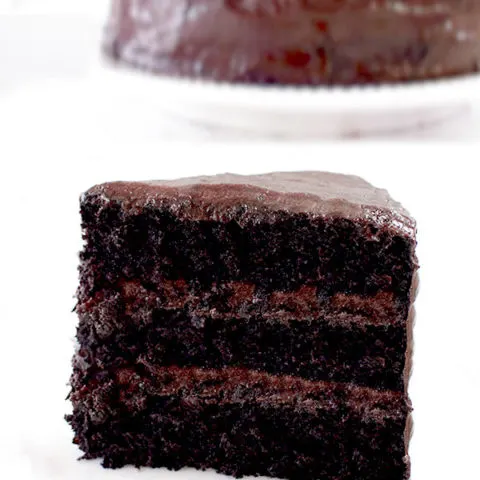 a slice of chocolate cake with a whole chocolate cake in the background