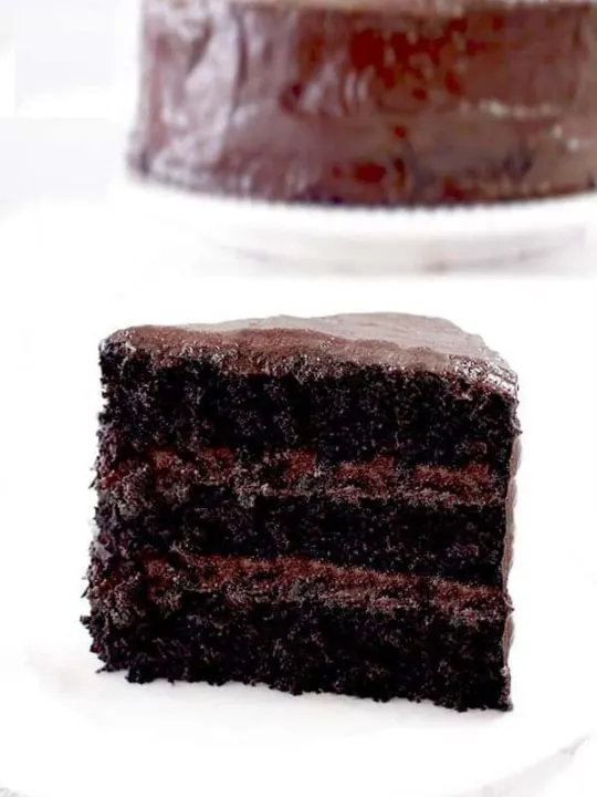 a slice of chocolate cake with a whole chocolate cake in the background