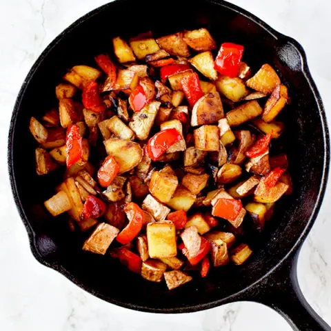 Breakfast hash of potatoes, peppers, and onions in a cast iron pan