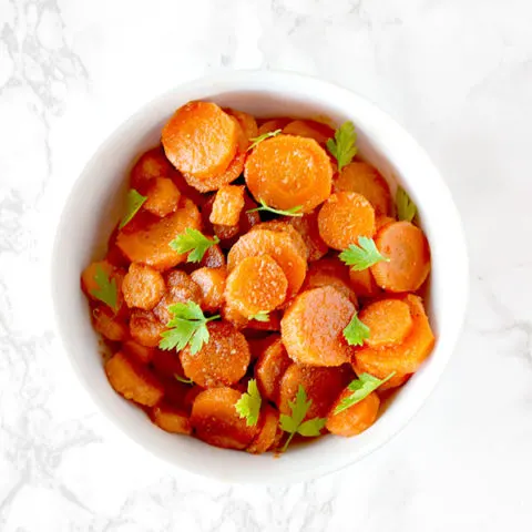 Moroccan carrot salad in a white bowl on a white marble counter