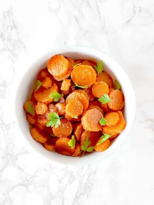 Moroccan carrot salad in a white bowl on a white marble counter