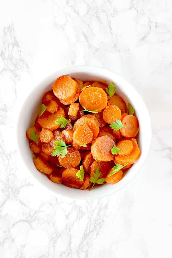 Moroccan carrot salad in a white bowl on a white marble counter