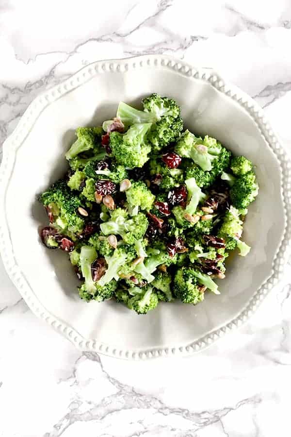 broccoli salad with cranberries and sunflower seeds in a white bowl on a white marble counter