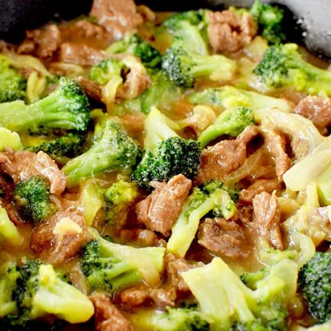 Beef and broccoli in a black pan on a white marble counter