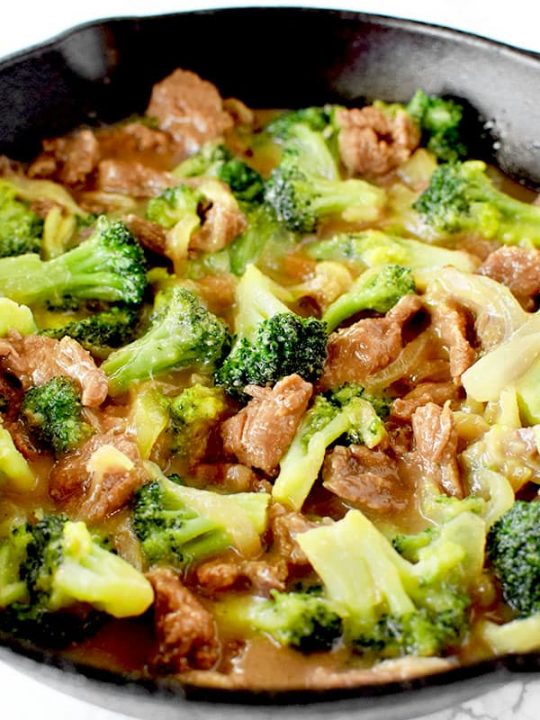 Beef and broccoli in a black pan on a white marble counter