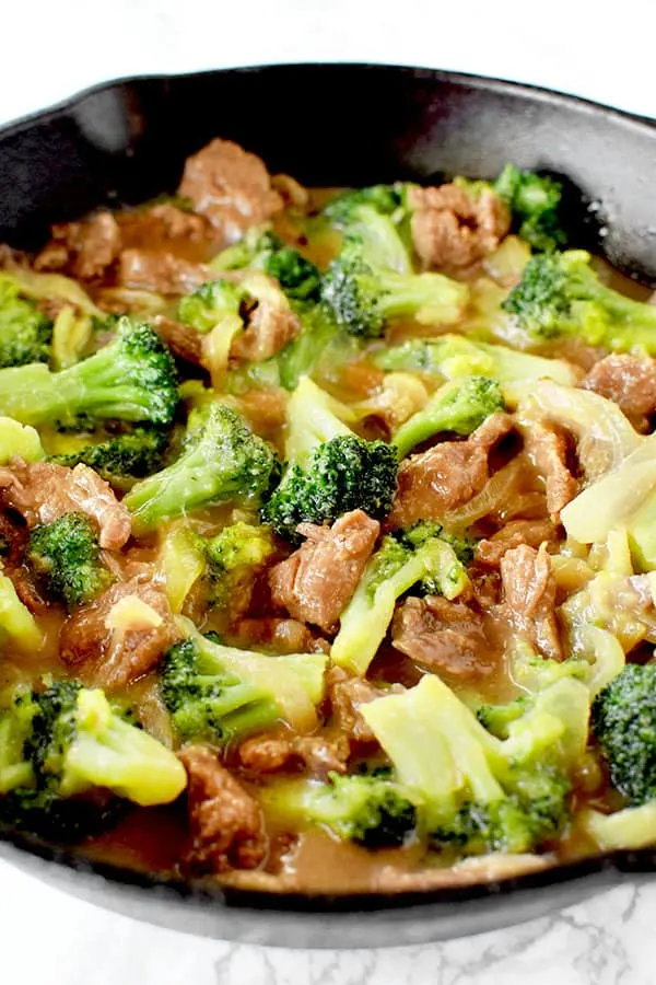 Beef and broccoli in a black pan on a white marble counter