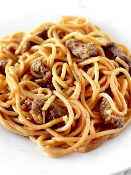 Beef lo mien on a white plate on a marble counter