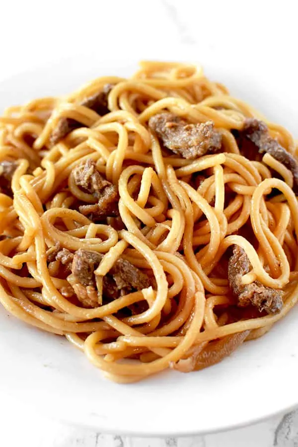 Beef lo mien on a white plate on a marble counter